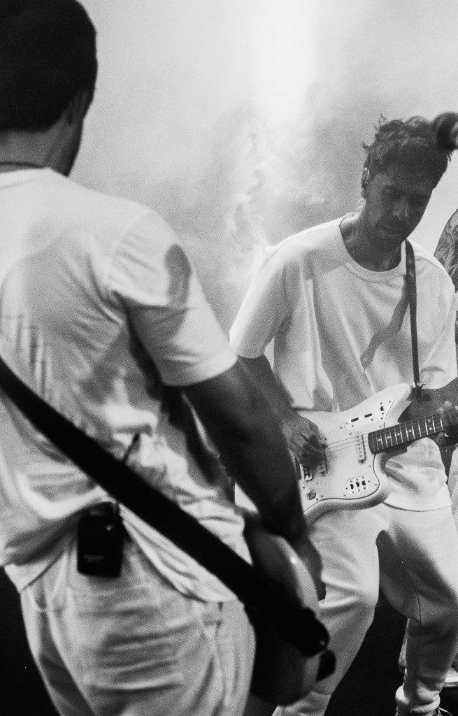 A Kool Kids no palco, em preto e branco, com fumaça e luz contra.